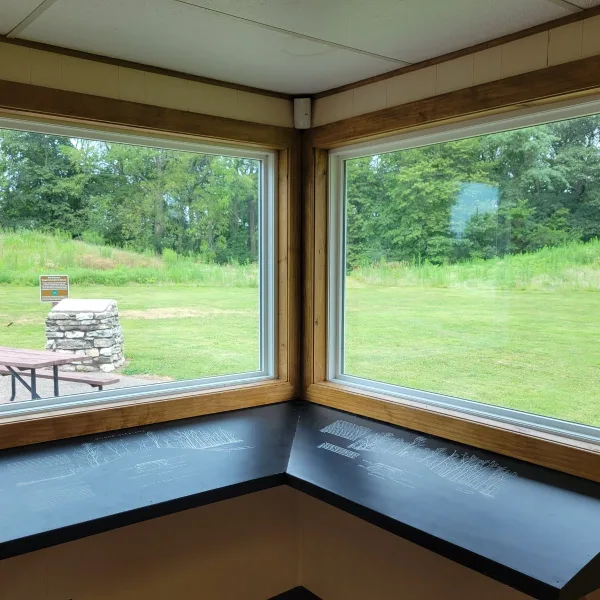 Toolesboro Mounds in Iowa, seen from inside the museum with exhibit panels, windows, open lawn, trees, and mounds visible outside.