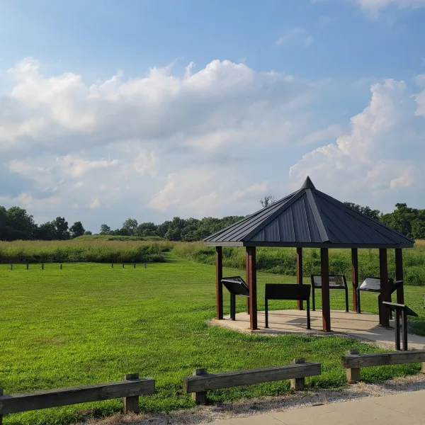 Towosahgy State Historic Site in Missouri, with an interpretive shelter, exhibit panels, open grass, and low Mississippian mounds in the background.