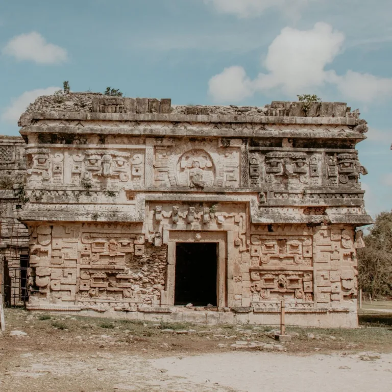 East Annex of Las Monjas at Chichén Itzá in Yucatán, Mexico, showing an ornate stone facade with Chaac masks and a central figure above the doorway.