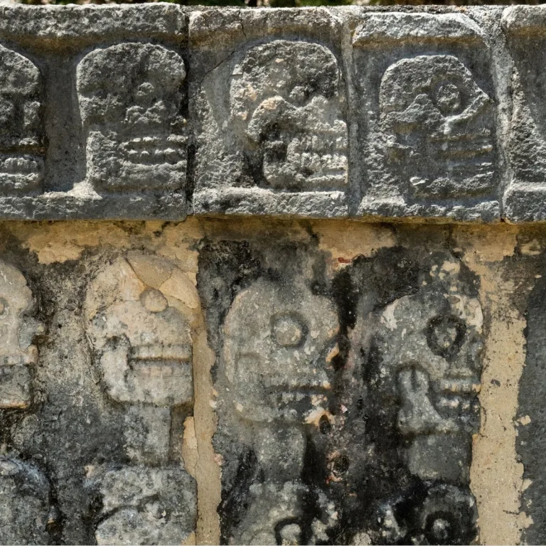 Close-up of weathered skull carvings on the Tzompantli, or Skull Platform, at Chichén Itzá in Yucatán, Mexico, showing two rows of limestone reliefs.
