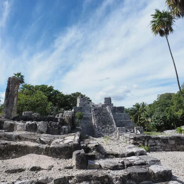 Wide view of El Castillo, Structure 1, surrounded by lower platforms, stone columns, and palm trees at El Meco in Quintana Roo, Mexico.