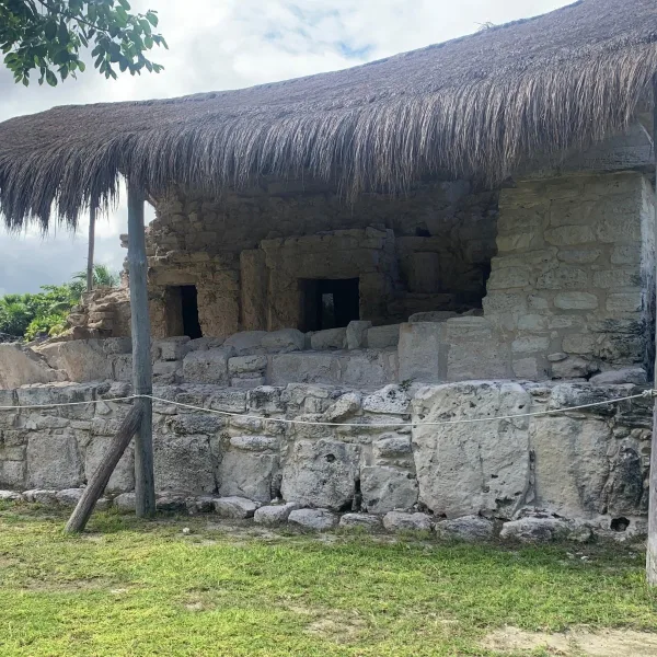 A Maya masonry building with multiple doorways stands beneath a protective thatched roof at El Rey in Cancún, Quintana Roo, Mexico.