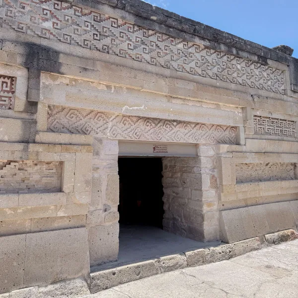 Stone facade in the Group of Columns at Mitla in Oaxaca, Mexico, with a doorway framed by geometric Zapotec mosaic fretwork panels and repeating stepped designs.