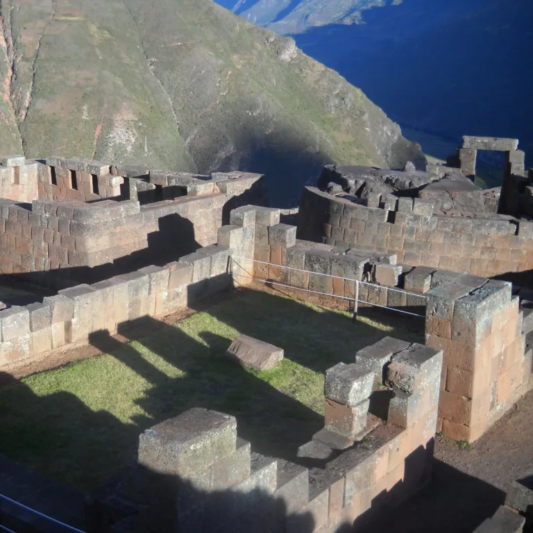 Fine Inca masonry in the Intihuatana sector at Pisac, Peru, with enclosed stone rooms and the Sacred Valley mountains beyond.