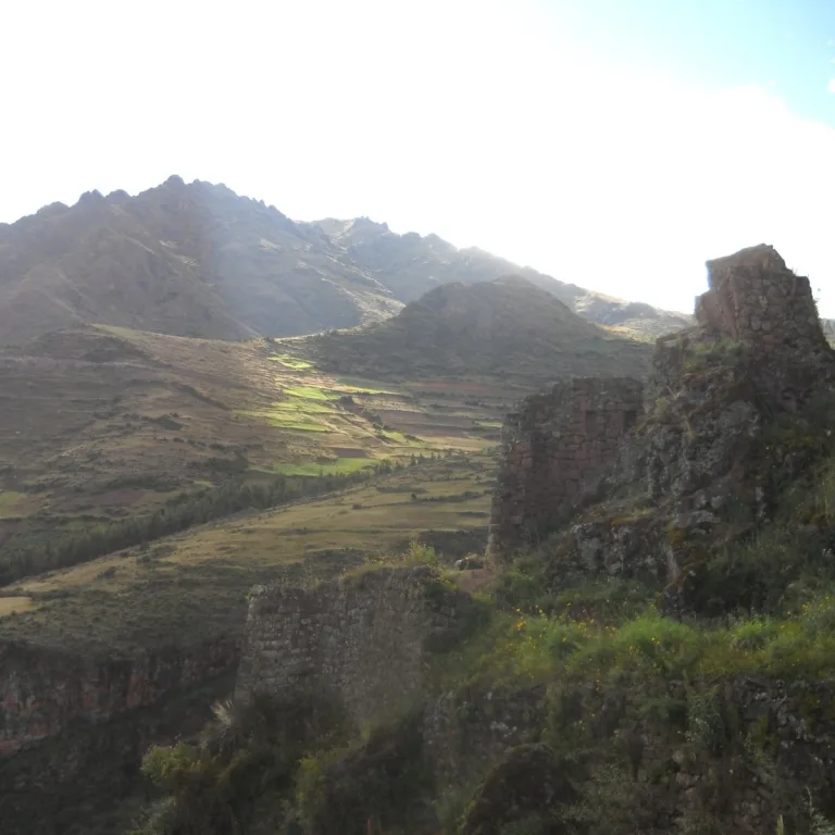 Weathered Inca stone ruins on the mountainside at Pisac in Cusco, Peru, overlooking terraced fields and rugged Andean peaks in late-day light.