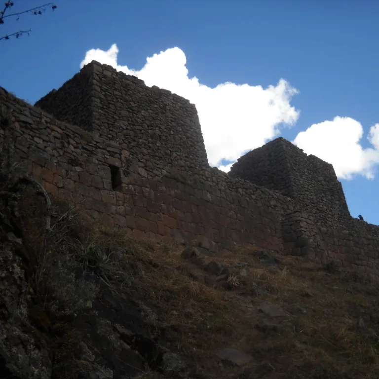 Stone walls of the Qallaqasa urban sector at Pisac in Cusco, Peru, rising along the steep mountainside beneath a blue sky.