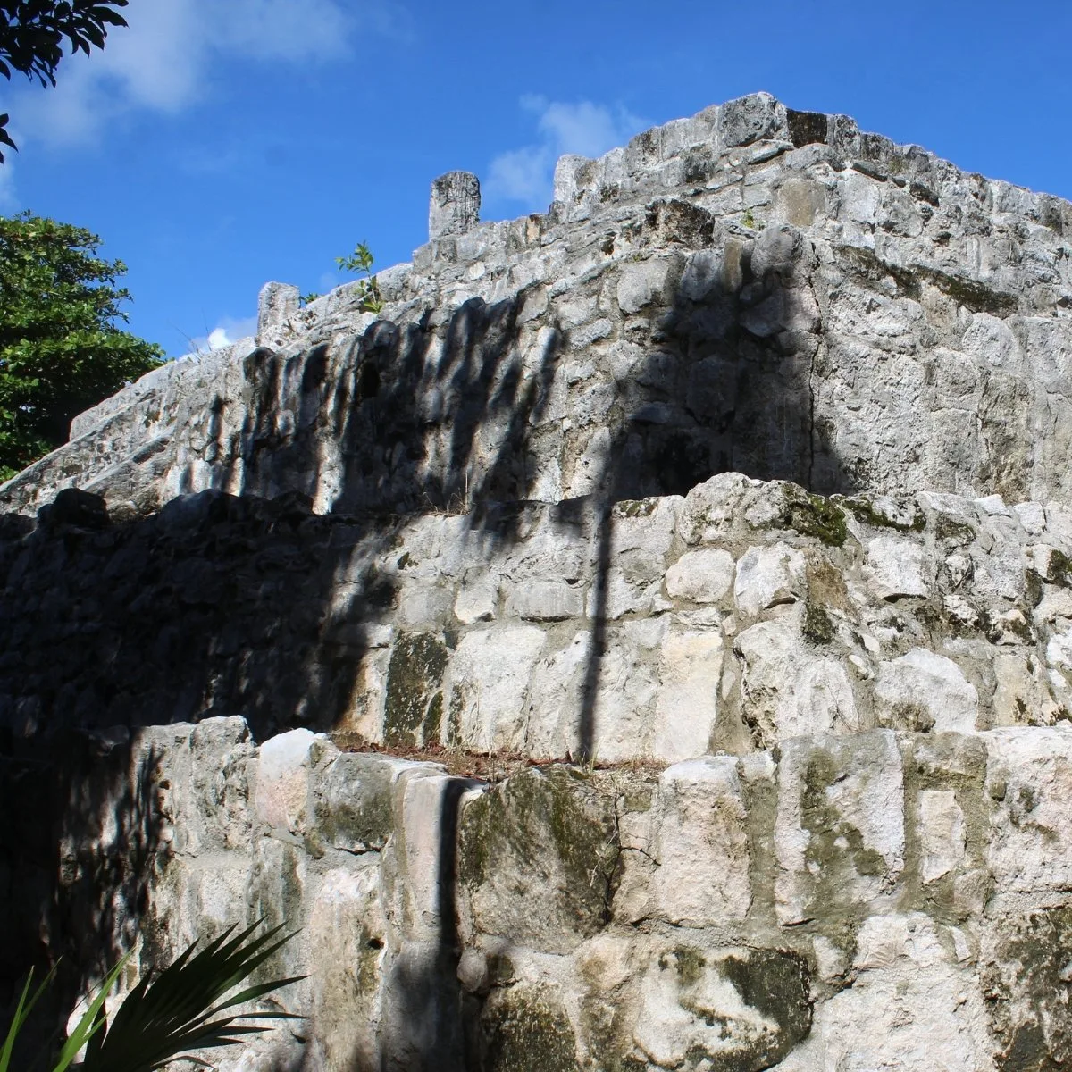Close view of the weathered masonry tiers and upper stone columns of the Main Pyramid at San Miguelito in Cancún, Mexico.
