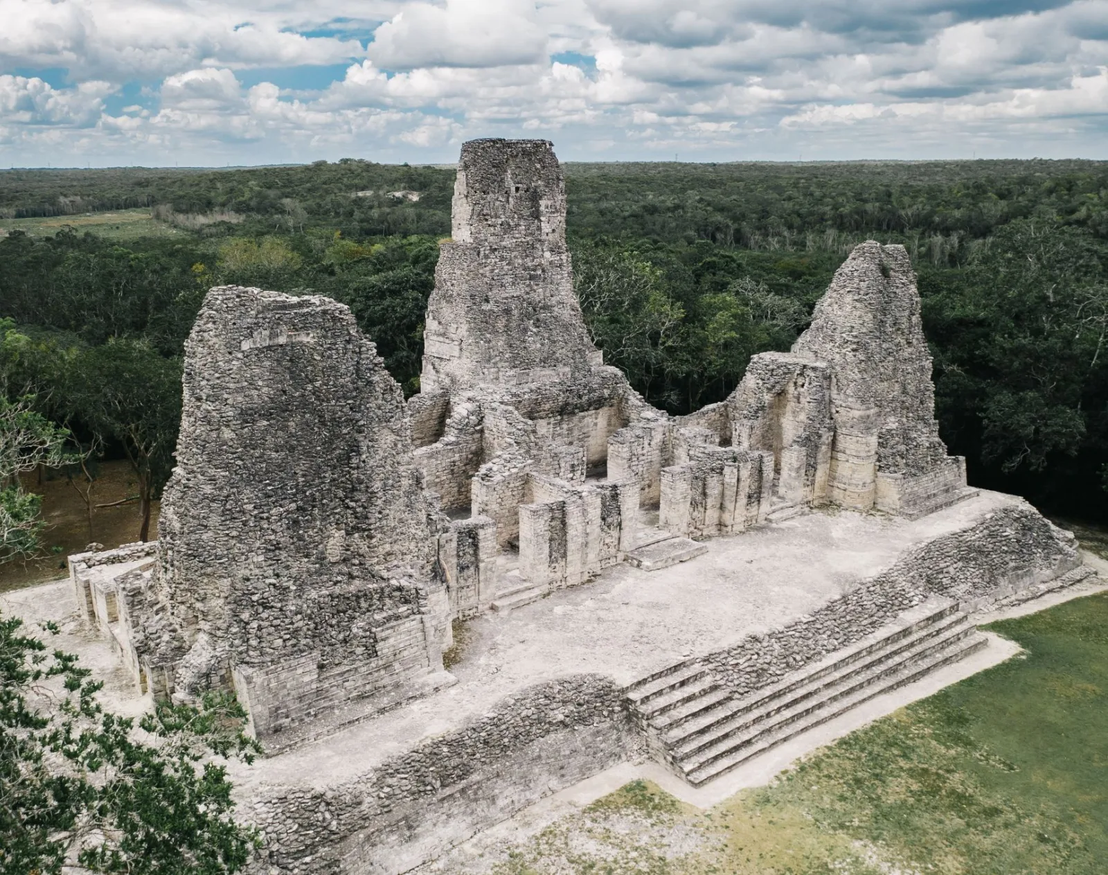 View of Structure I-1, the Building of the Three Towers at Xpuhil in Campeche, Mexico, showing all three Río Bec-style masonry towers, the central rooms, raised platform, and front stairway surrounded by forest.