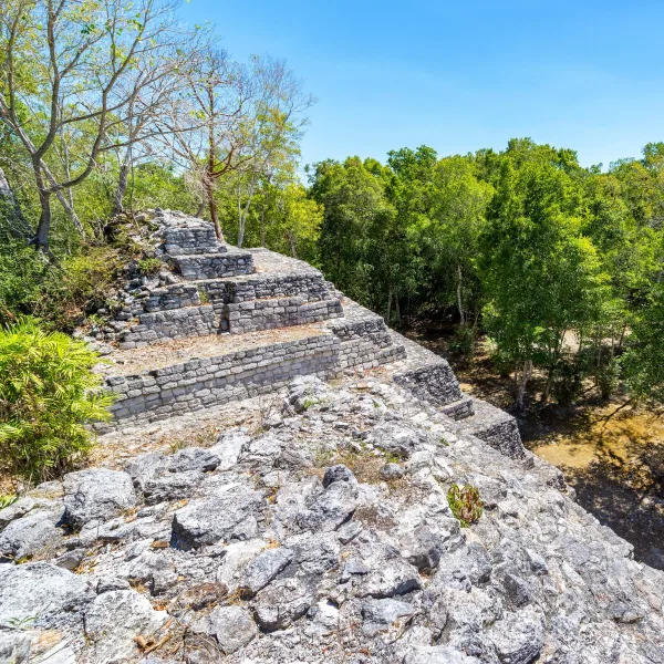 Elevated view of a stepped Maya pyramid at Balamkú in Campeche, Mexico, showing successive limestone terraces, weathered masonry, and dense tropical forest surrounding the structure.