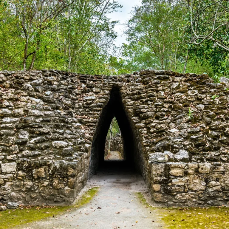 The Pasadizo Abovedado at Becán, with a narrow corbel-vaulted opening through stone masonry and daylight at the far end.