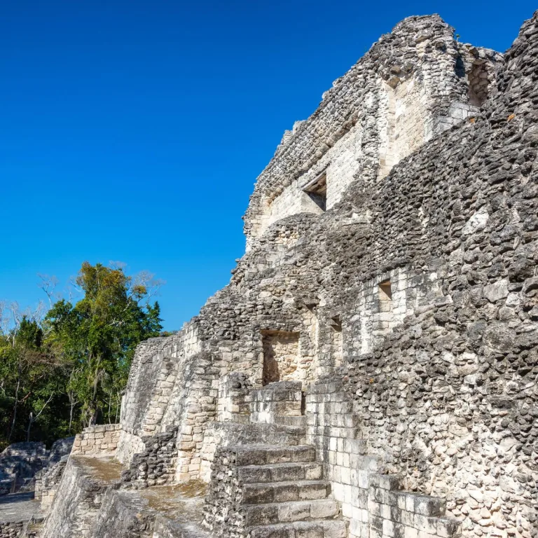 Angled view of Structure X at Becán, showing stone steps, openings on several levels, and the surviving upper façade.