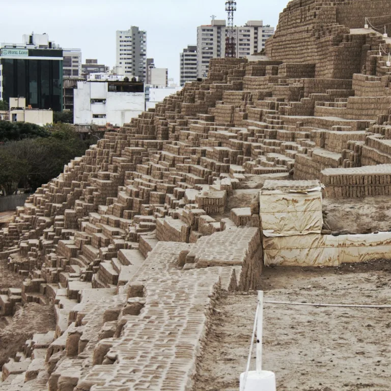 The Gran Pirámide at Huaca Pucllana in Miraflores, Lima, showing its extensive stepped adobe terraces with modern city buildings rising behind the archaeological site.