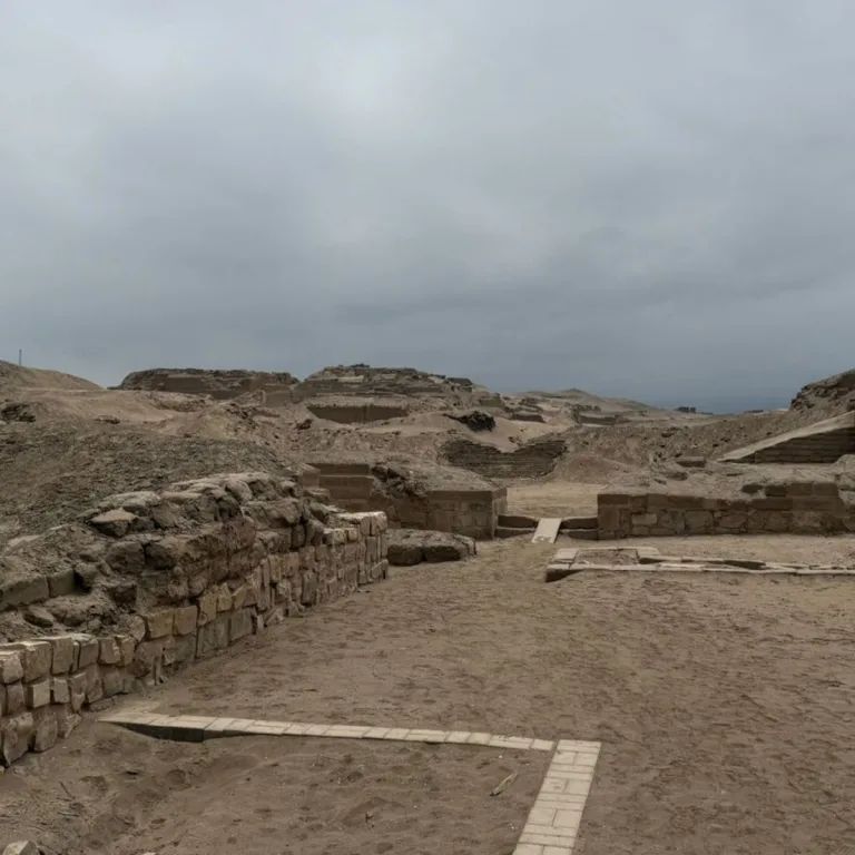 Low stone walls and sandy excavated enclosures at Pachacamac, Peru, beneath an overcast sky.