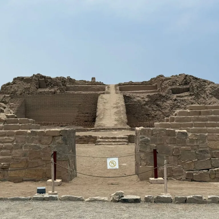 A central earthen ramp climbs an adobe platform at Pachacamac, viewed through a stone-walled entrance.