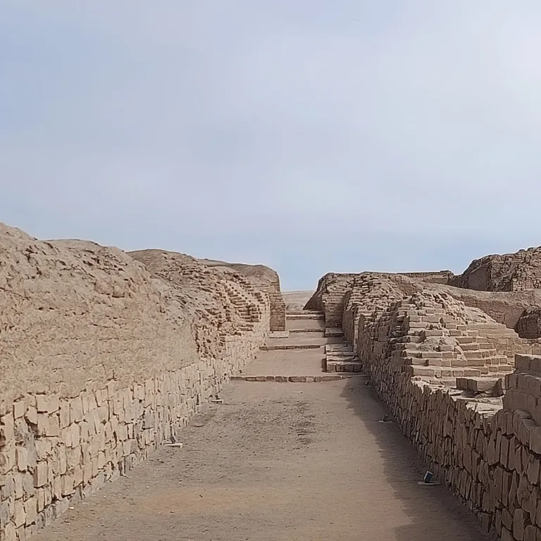 A long sandy passage at Pachacamac runs between stone foundations and weathered adobe walls, with low steps across its floor.